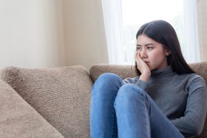 Close up face of unhappy Asian pretty young woman siting alone on couch with feeling sadness , emotional young woman was depressed on sofa