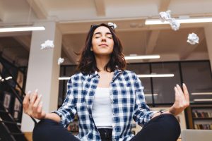 Relaxing time joyful young brunette woman having meditation on table in office surround flying papers. Taking a break, pause, smart student, relaxation, great success, dreaming
